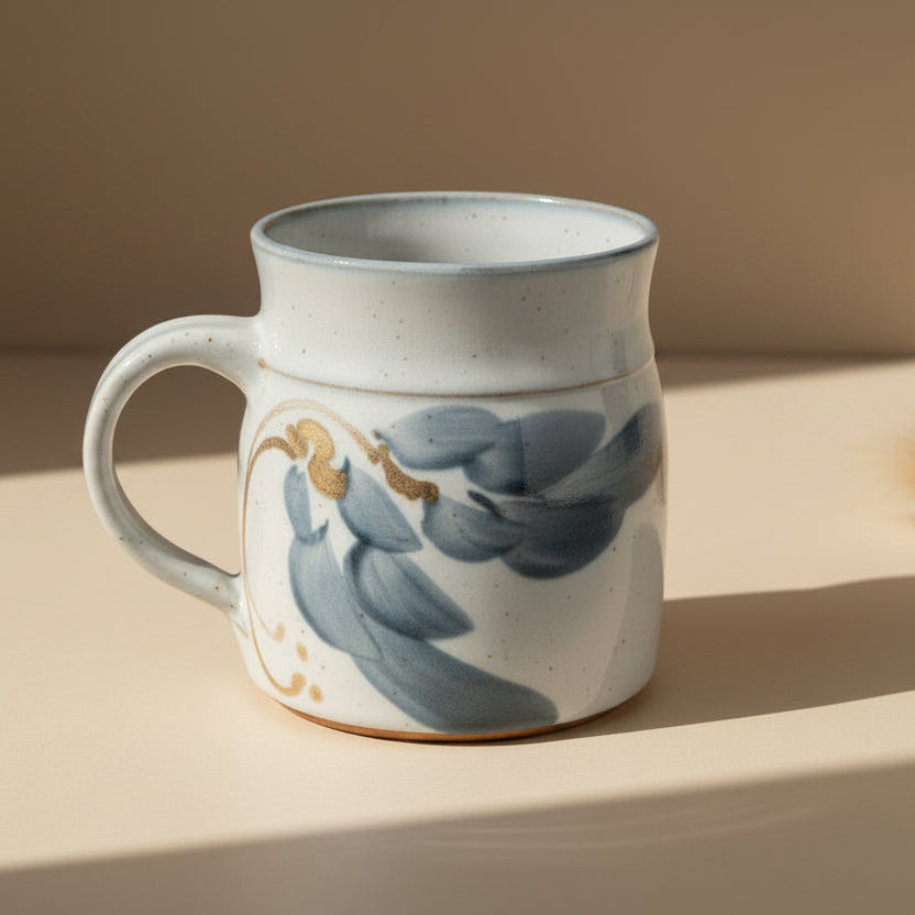 A handmade ceramic mug with a blue and floral design on a speckled white glaze