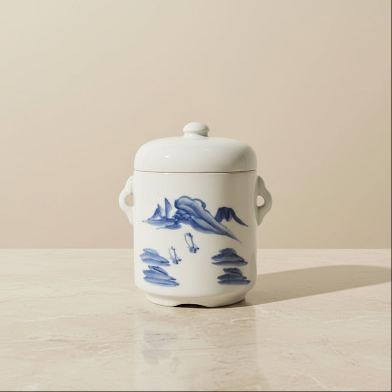 A white ceramic lidded jar with blue landscape illustrations.