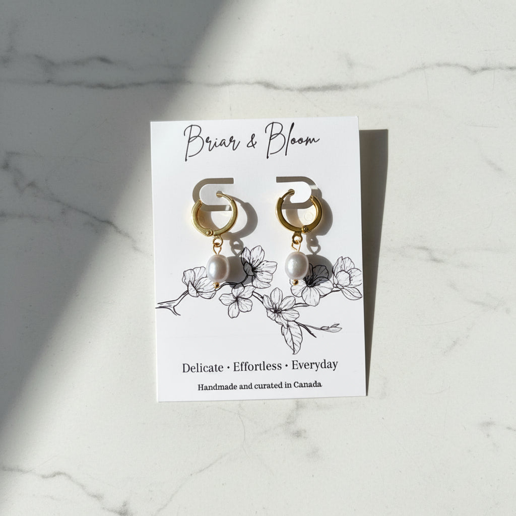 A pair of gold hoop earrings with silvery grey pearl drops.