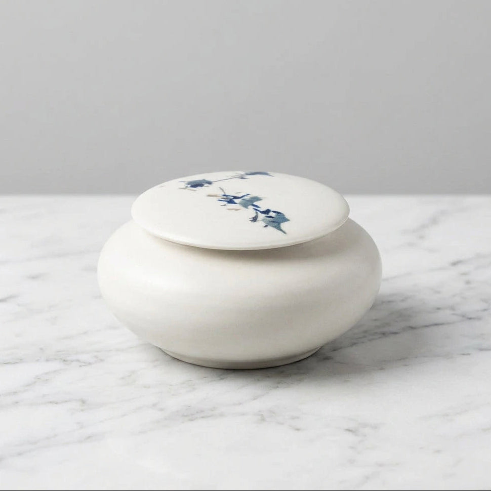 A small round white ceramic lidded box with blue floral illustrations on the lid.