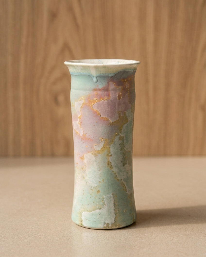 A tall, flared ceramic vase with a marbled glaze in pastel green, pink, cream, and gold.