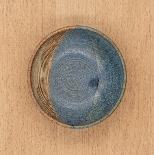 A handmade ceramic bowl with a textured, speckled glaze in shades of blue, and brown.
