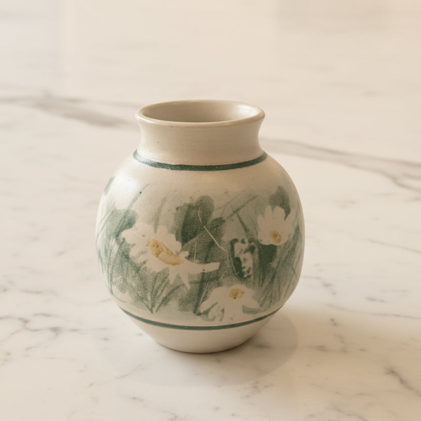 A small handmade ceramic vase with painted daisies and green leaves.