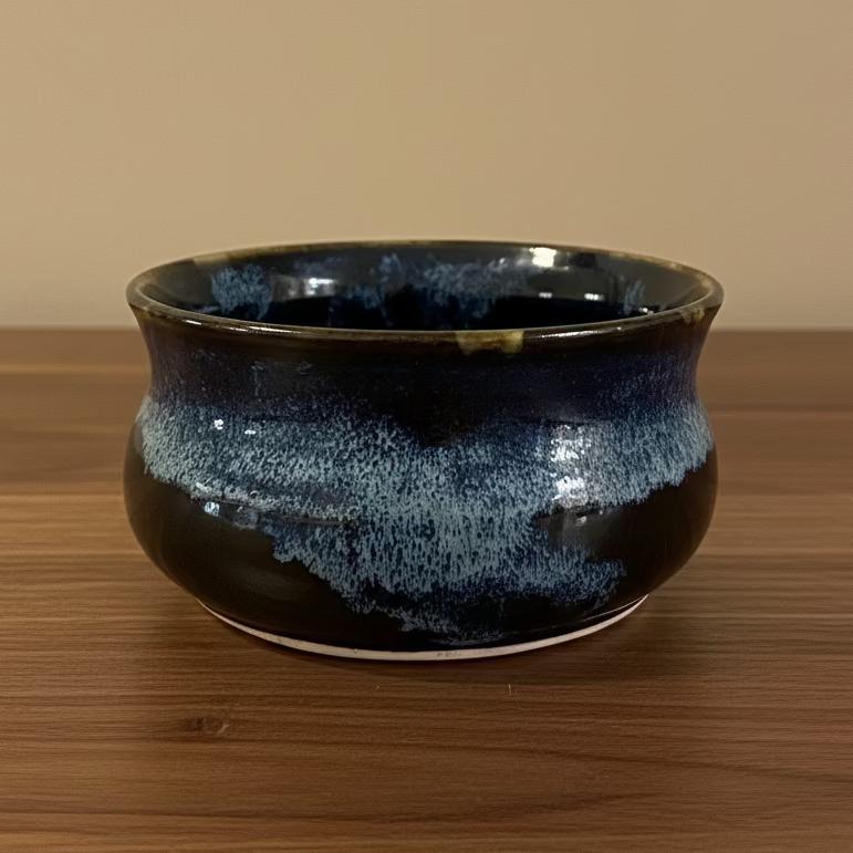 Asmall ceramic bowl with a glossy dark blue and black glaze featuring a subtle speckled pattern
