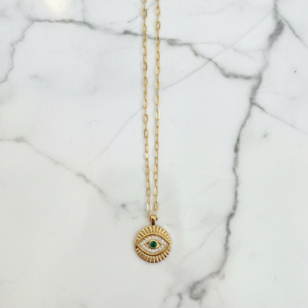 Gold necklace with an evil eye pendant on a marble surface