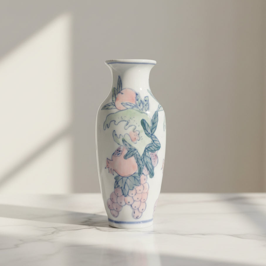 A white ceramic vase decorated with hand-painted a pink peache, pomegranate, grapes and green leaves