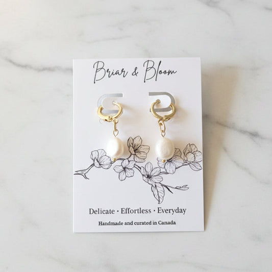 A pair of gold hoop earrings with white pearl drops.