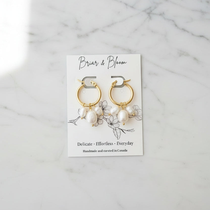 Gold hoop earrings with small white pearl-like drops.