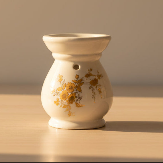 A small ceramic wax Melter with a white body decorated with golden floral patterns.