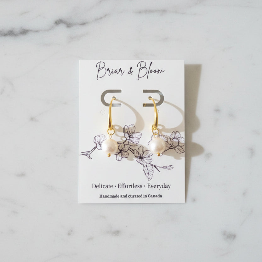 A pair of gold earrings with small white bead drops.