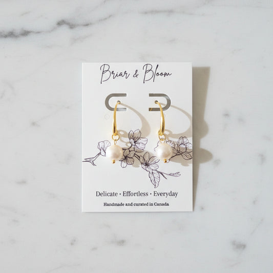 A pair of gold earrings with small white bead drops.