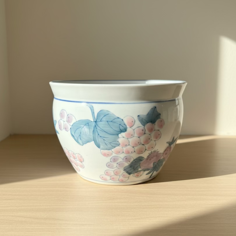 A white ceramic planter pot decorated with blue leaves and grapes