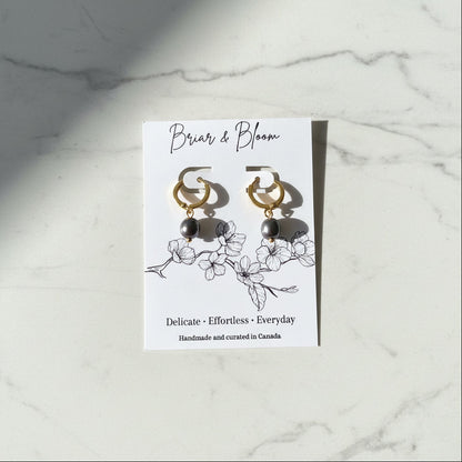 A pair of gold hoop earrings with dark blue grey pearl drops.