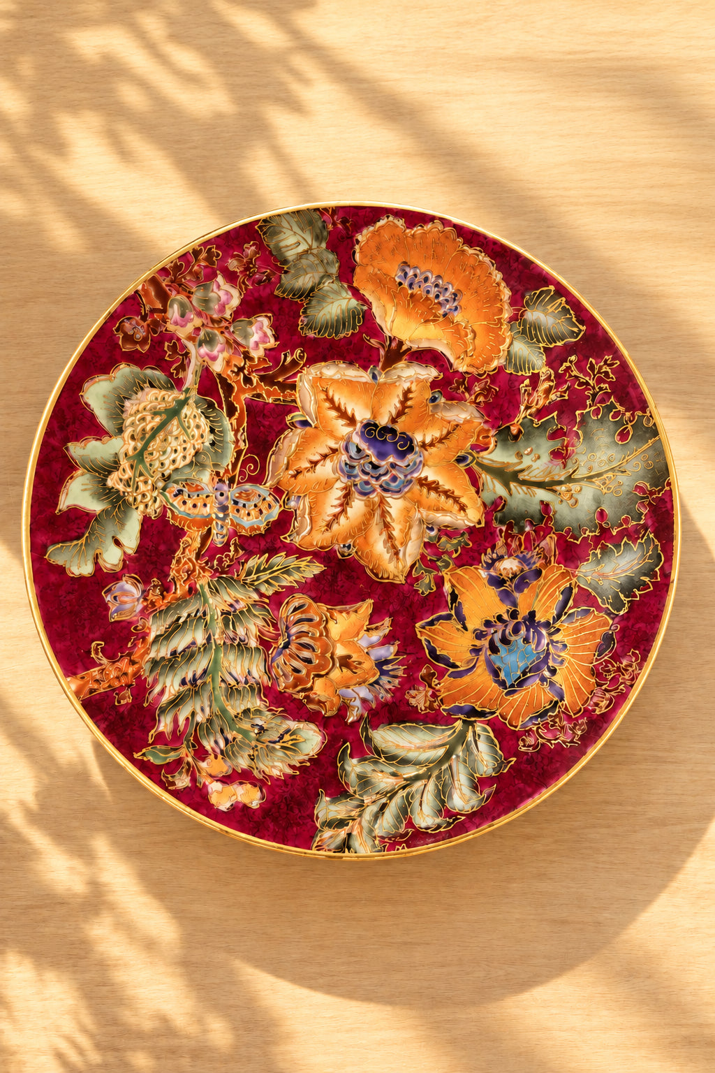 A round decorative plate with a rich red velvet-like background and intricate multicolor floral embroidery.