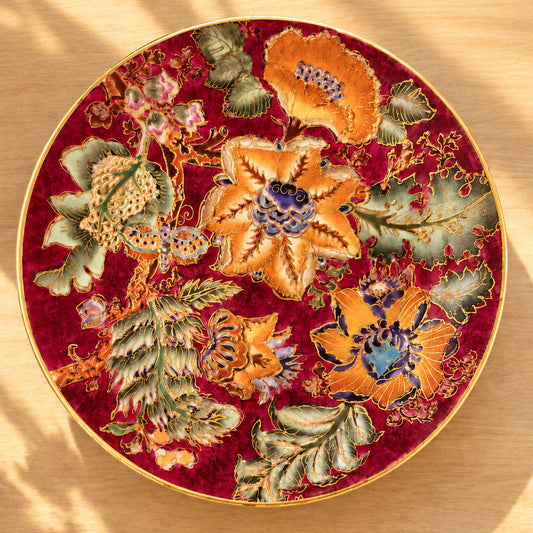 A round decorative plate with a rich red and intricate multicolor floral detauls. 