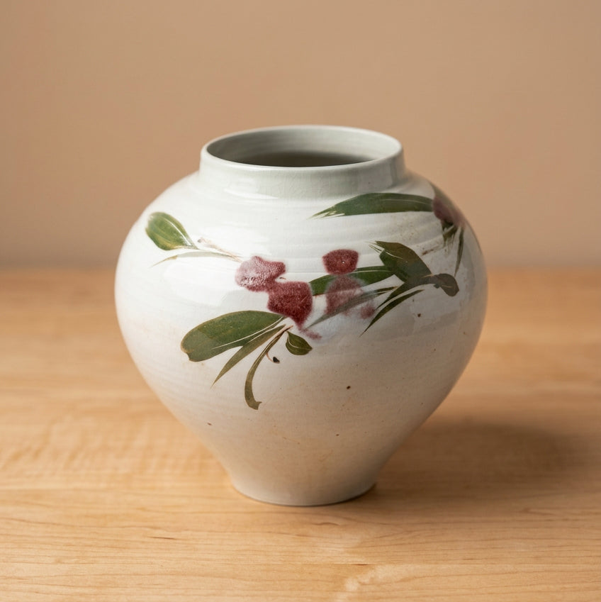 A round ceramic vase with a glossy white glaze, decorated with painted green leaves and reddish-brown berries.