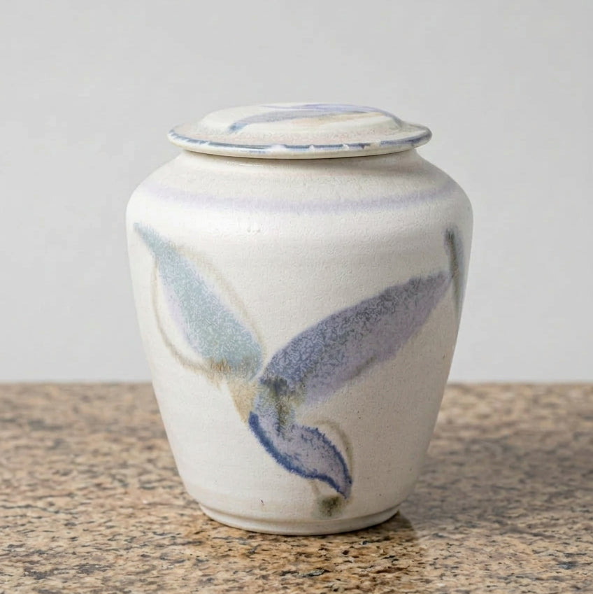 A handmade ceramic lidded jar with a white glaze and blue brushstroke patterns.