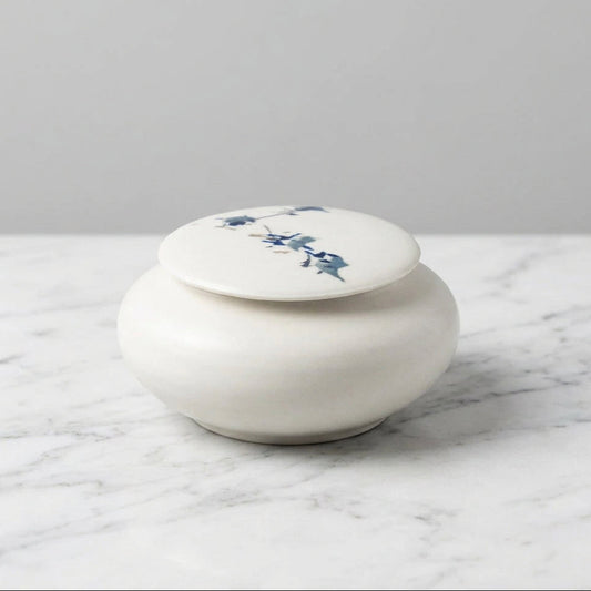 A small round white ceramic lidded box with blue floral illustrations on the lid.