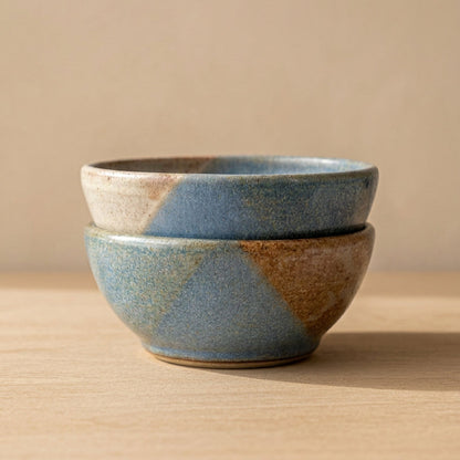 A handmade ceramic bowl with a geometric faceted pattern in blue and brown glaze.