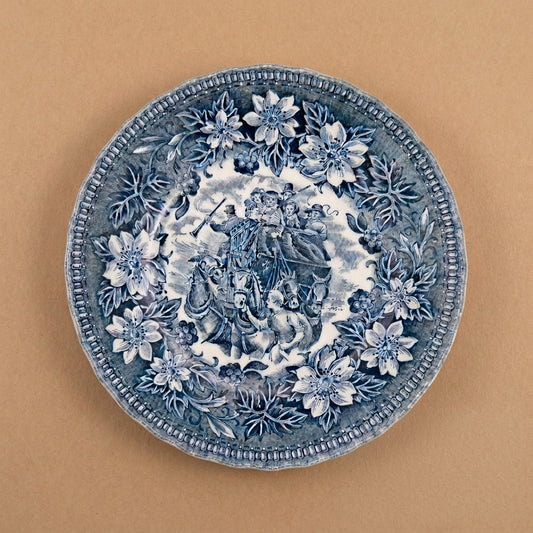 A round blue and white embossed ceramic plate or dish with floral borders and a central classical scene