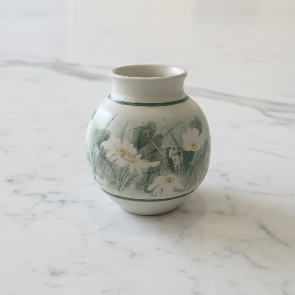 A small handmade ceramic vase with painted daisies and green leaves.
