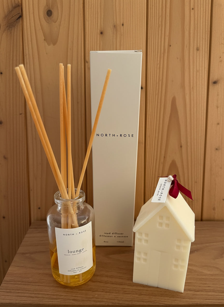 Diffuser bottle with reeds, box, and house-shaped candle on a wooden surface