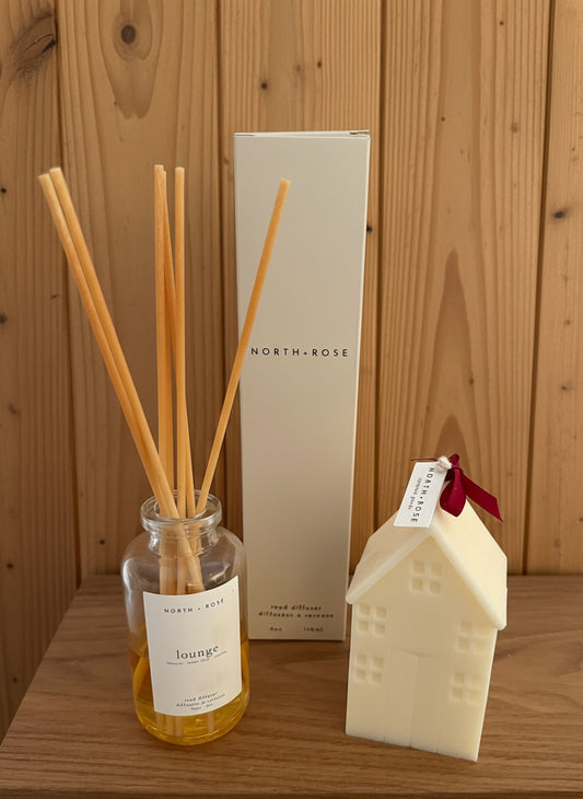 Diffuser bottle with reeds, box, and house-shaped candle on a wooden surface
