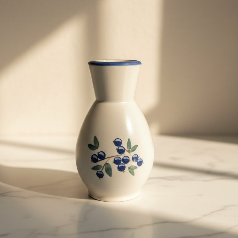 A white ceramic vase with a blue rim, decorated with a blueberry and green leaf motif