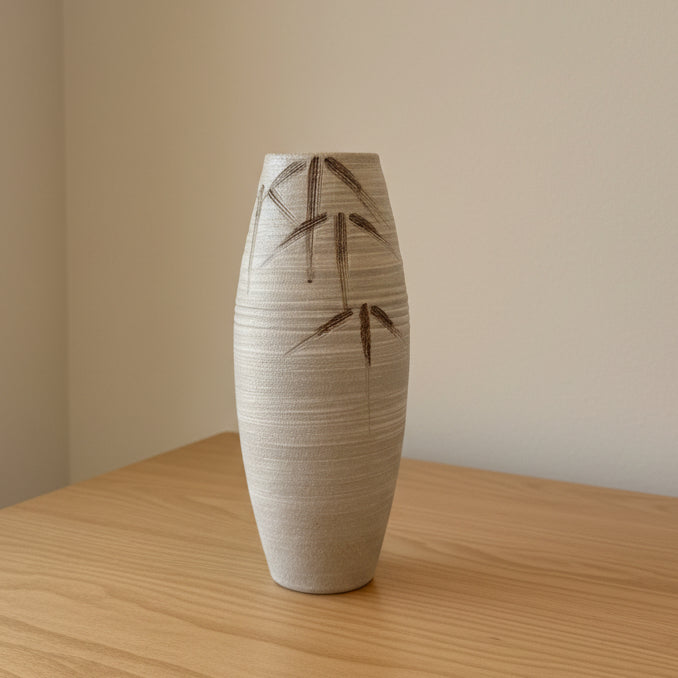 A tall, ribbed ceramic vase with a textured cream finish and dark bamboo leaf patterns