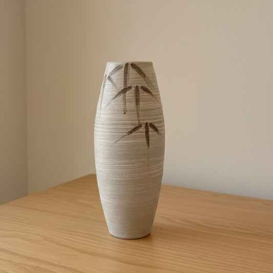 A tall, ribbed ceramic vase with a textured cream finish and dark bamboo leaf patterns