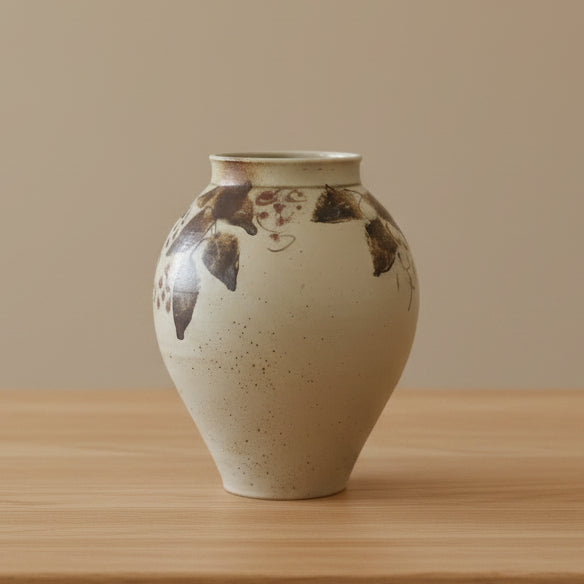 A handmade ceramic vase with a rounded body, flared rim, and hand-painted rustic patterns in brown, black, and small red floral details