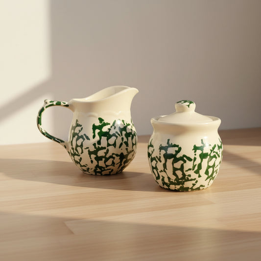A ceramic pitcher and matching sugar bowl with a lid, both decorated with a green spongewear pattern on a cream glaze