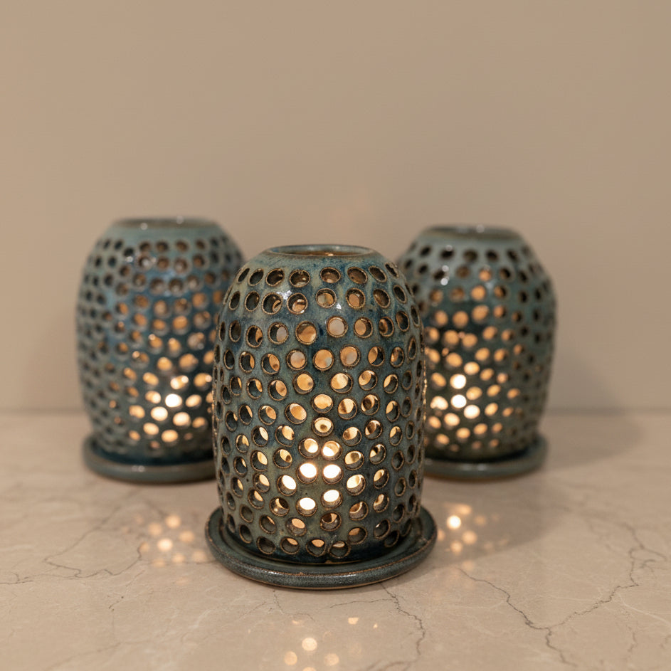 Three decorative glass candle holders with a perforated pattern, lit with warm lights 