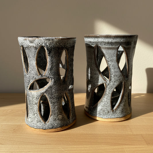 Two ceramic candle holders with leaf-shaped cutouts, featuring a speckled gray and black glaze with a natural clay base