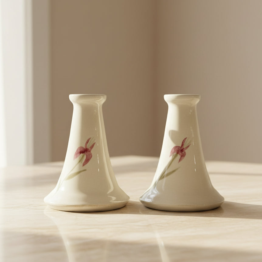 A pair of small beige ceramic candle holders with pink floral designs