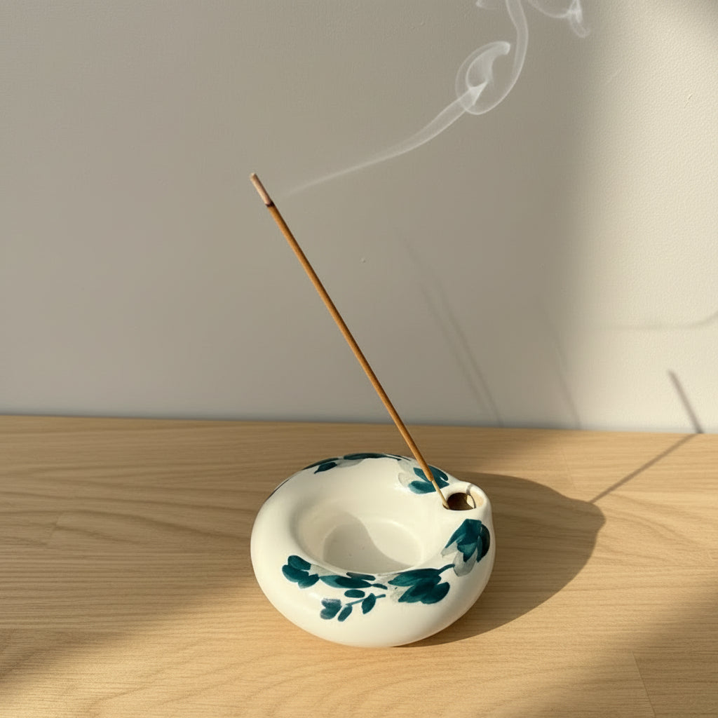 A small white ceramic incense holder with dark teal floral patterns