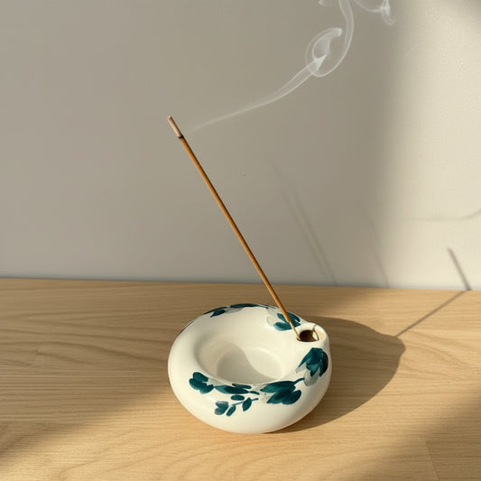 A small white ceramic incense holder with dark teal floral patterns