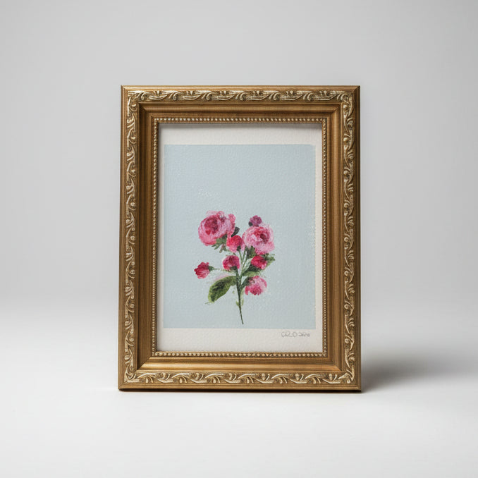 A framed floral art print featuring pink and roses with green leaves on a pale blue background, set in an ornate gold frame