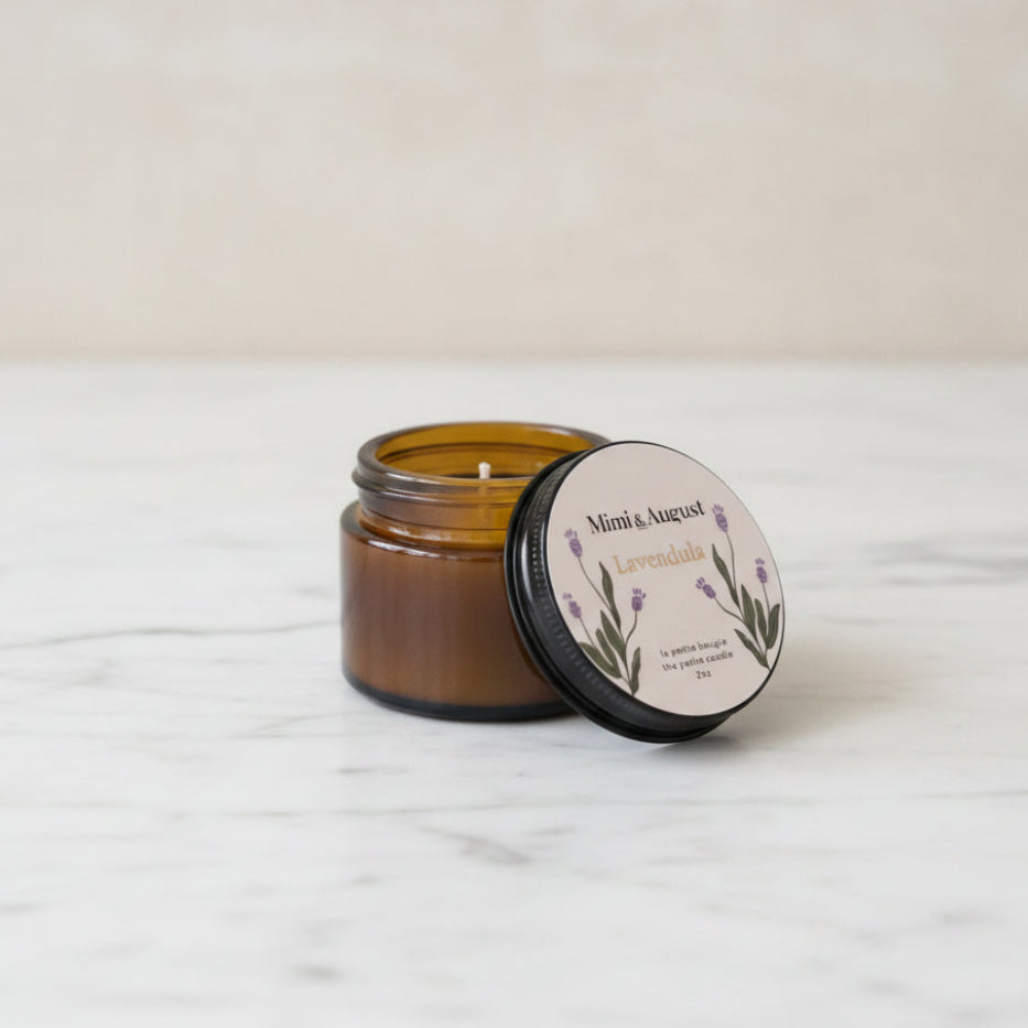 An amber glass jar candle with its black lid off, showing the wax and wix.