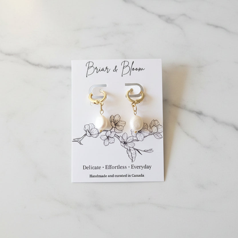 A pair of gold hoop earrings with white pearl drops.