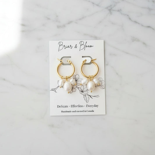 Gold hoop earrings with small white pearl-like drops.