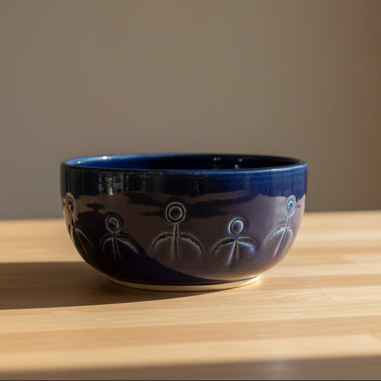 A dark blue ceramic bowl with white hand-painted people motifs.