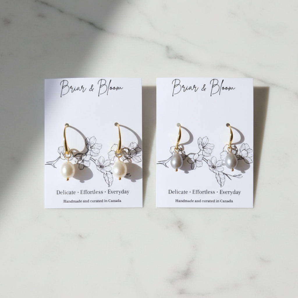 A pair of gold earrings with small white and grey bead drops.