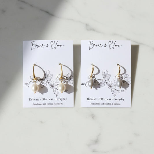 A pair of gold earrings with small white and grey bead drops.