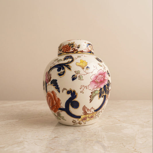 A white ceramic lidded jar decorated with colorful hand-painted floral motifs, including pink, orange, yellow, and blue flowers and leaves.