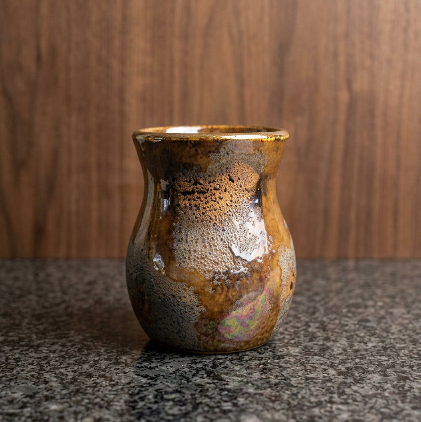 A small handmade ceramic vase with a textured, speckled glaze in earthy brown, gold, and silver tones.