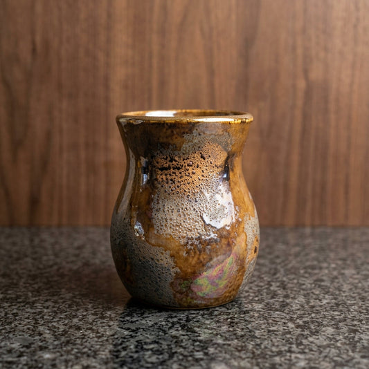A small handmade ceramic vase with a textured, speckled glaze in earthy brown, gold, and silver tones.