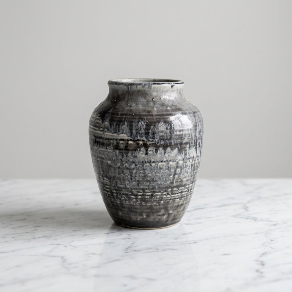 A small ceramic vase with a textured, mottled glaze in charcoal gray, black, and white.