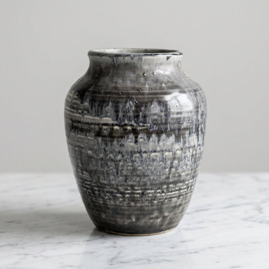 A small ceramic vase with a textured, mottled glaze in charcoal gray, black, and white.