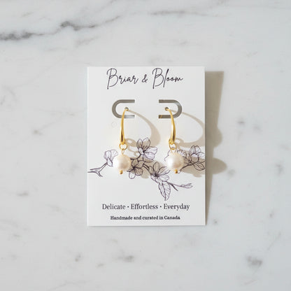 A pair of gold earrings with small white bead drops.